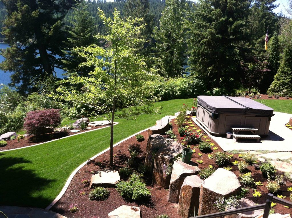 Landscape beds freshly covered in bark around boulders, shrubs and a hot tub patio in the Inland Northwest